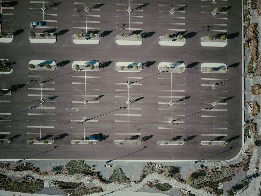 Drone aerial view of an empty parking lot with trees and shadows, creating a geometric pattern.