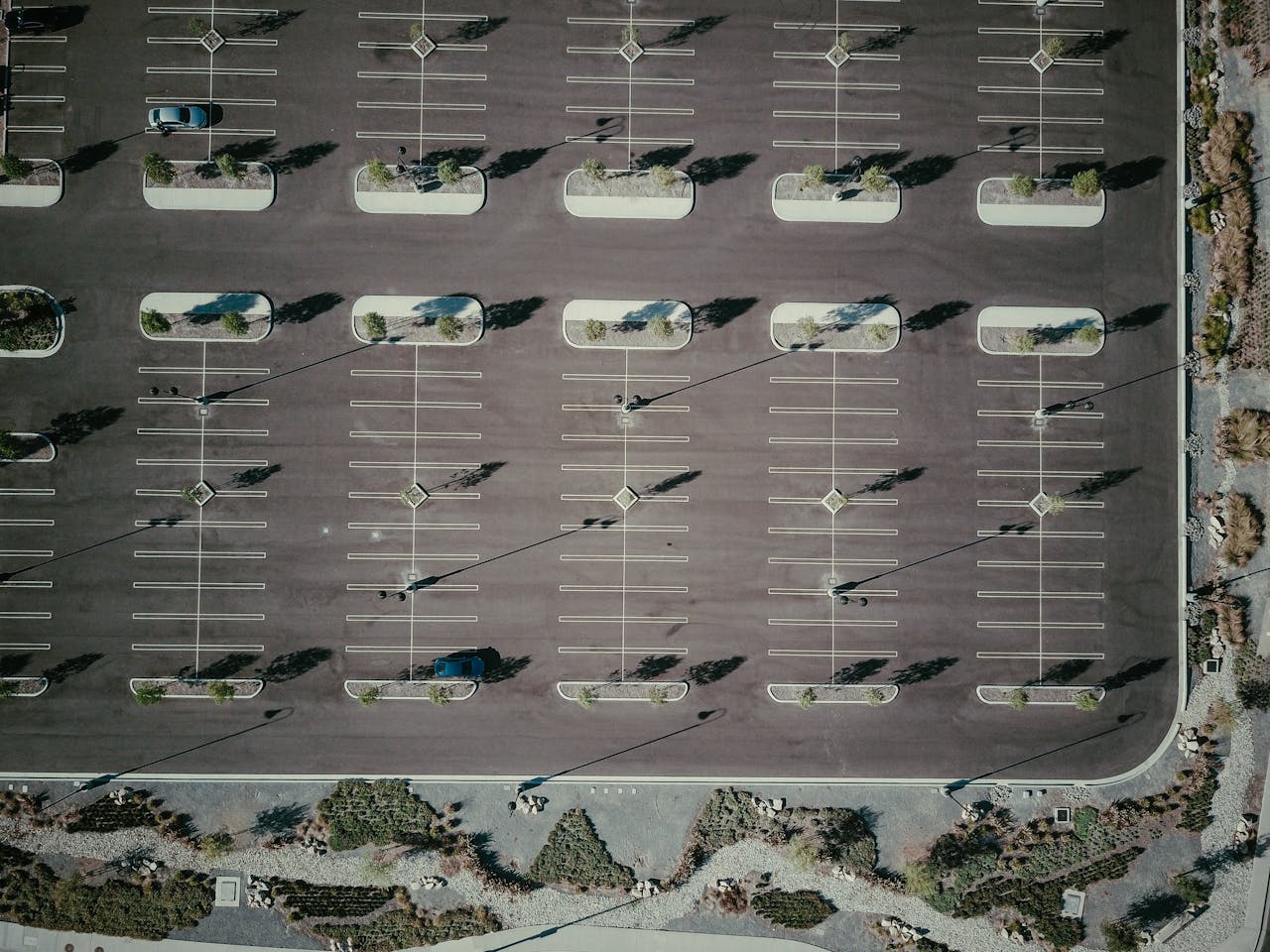 Drone aerial view of an empty parking lot with trees and shadows, creating a geometric pattern.
