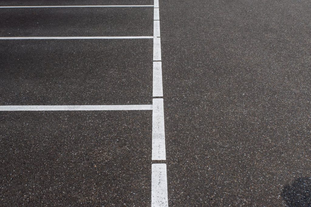 Asphalt parking lot showing white lines marking parking spaces. Minimalist urban scene.