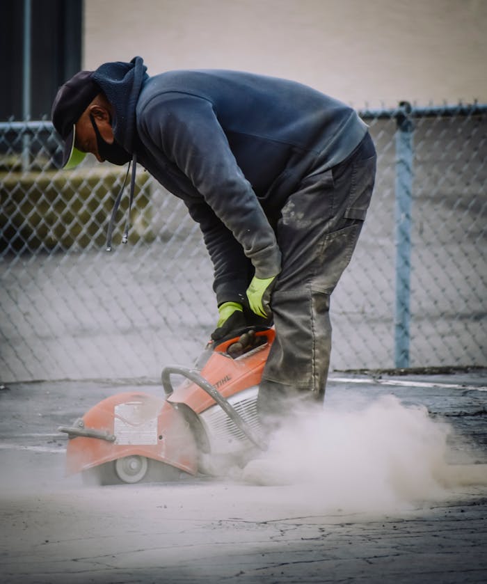 Worker with protective gear cutting concrete with a saw in an outdoor setting.